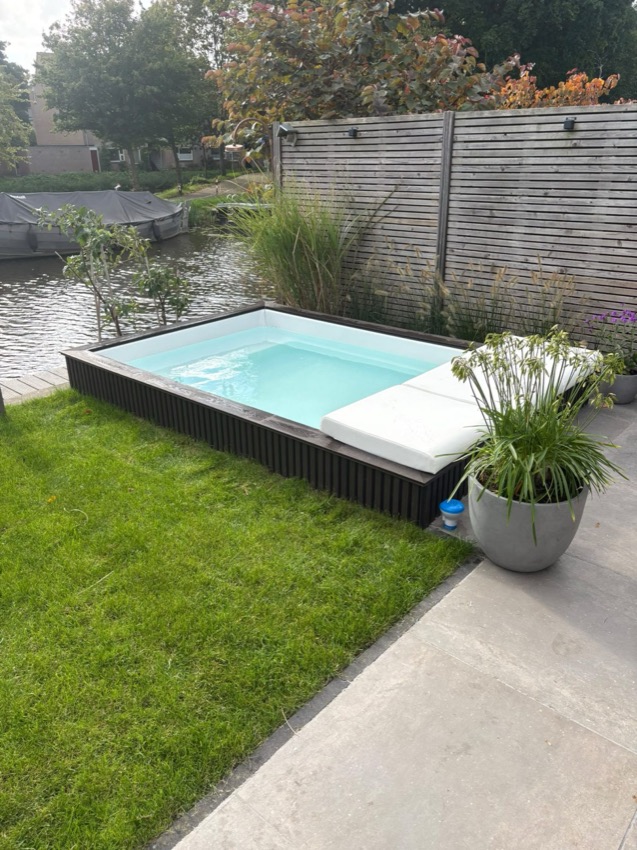 Minipool met donkere buitenbekleding, lichte rand en een plantenpot bij de tuin aan het water.